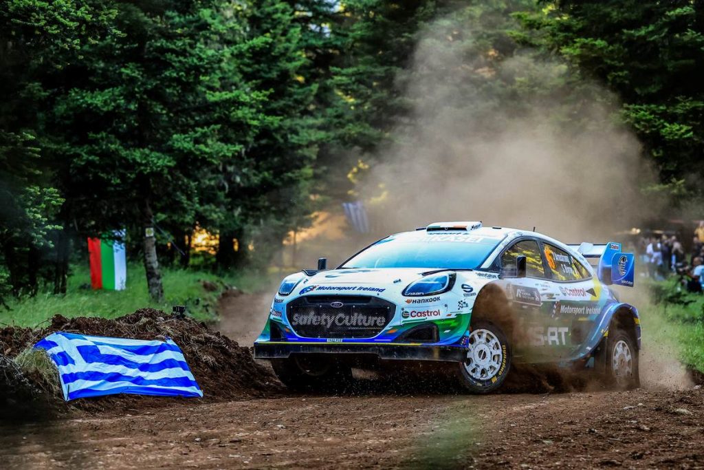 Jon Armstrong and Shane Byrne power their M-Sport Ford Puma Rally1 through a dusty forest gravel stage past a Greek flag at Acropolis Rally Greece 2026